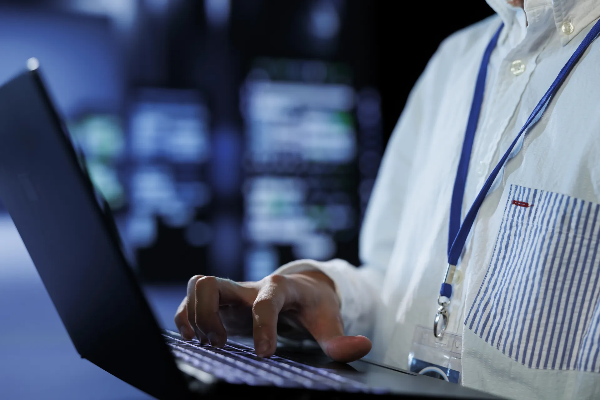 Tech support in data center uses laptop to prevent system overload during peak traffic periods. Hardworking expert in server farm ensuring enough network bandwidth for smooth operations, close up